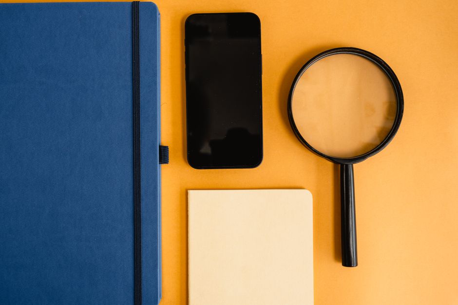 A flat lay of a journal, smartphone, and magnifying glass on a vibrant yellow background.